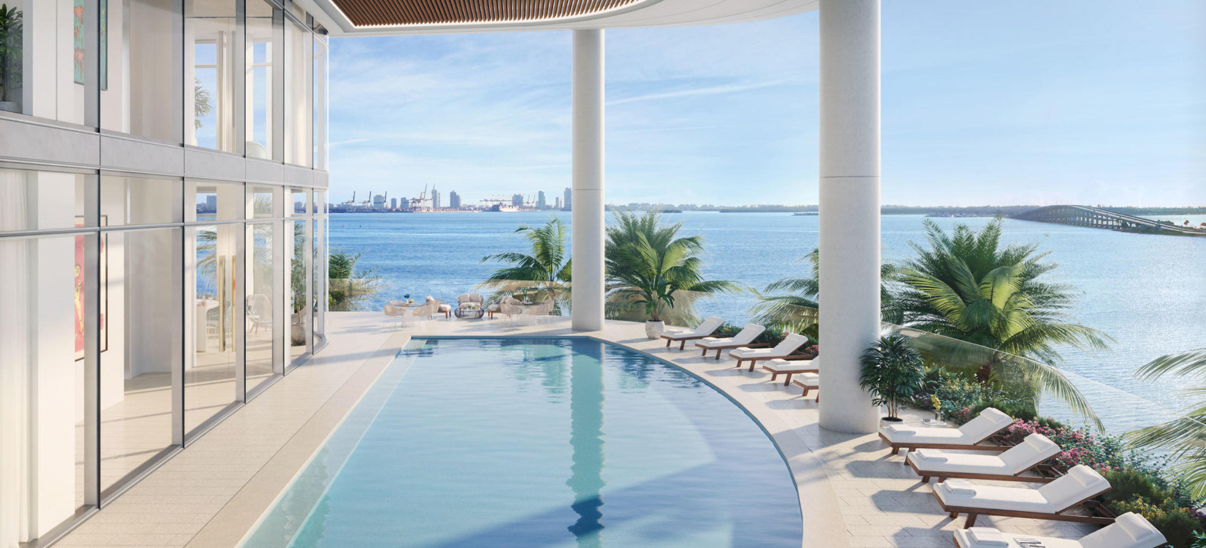 Infinity-edge bayfront pool at UNA Residences Miami overlooking Biscayne Bay and the Miami skyline with lounge chairs and tropical palm trees