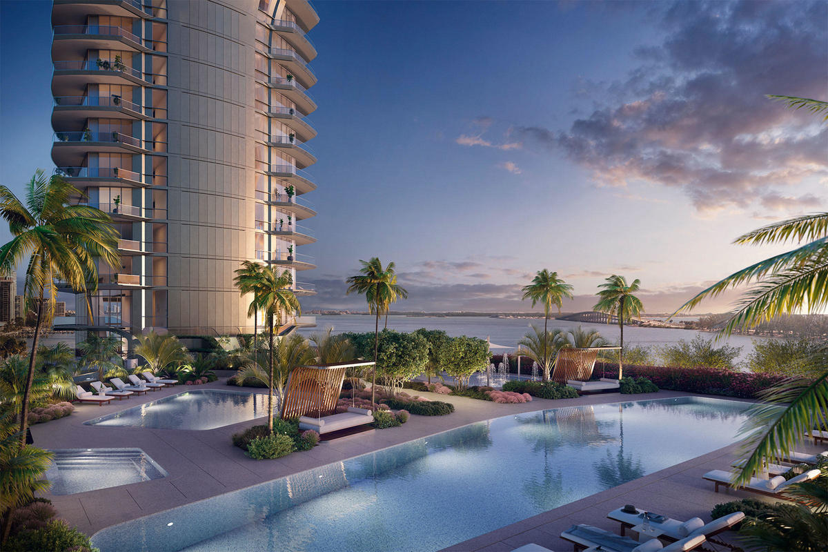 Sunset resort-style pool deck at UNA Residences Miami with palm trees, lounge seating and expansive Biscayne Bay waterfront views